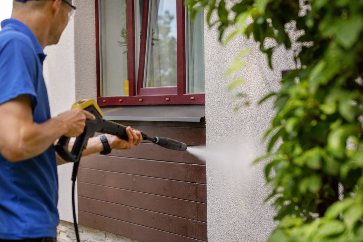 Technician using a pressure washer to clean a house